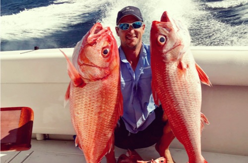 Fisherman holding two large sports fish caught on a Kokomo Private Island Fiji fishing trip.