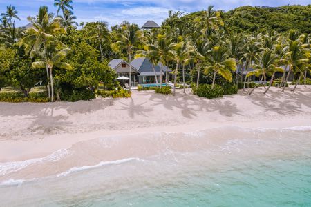 A beachfront villa nestled amongst lush greenery, overlooking a wide, pristine beach and clear blue waters at Kokomo Island Fiji.