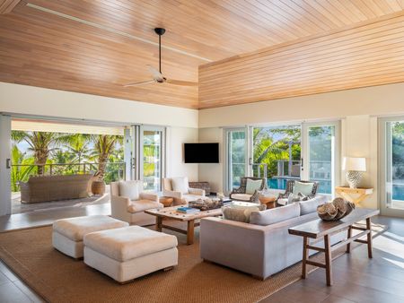 The living area of a residence at Kokomo Island Fiji, with several lounges and armchairs surrounding a wooden coffee table. The room has modern wood panelling on the high ceilings and is surrounded by full-height sliding doors, through which the residence’s deck and pool can be seen.