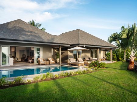 The exterior of a residence and its surrounding lawns at Kokomo Island Fiji. Several deck chairs line sit next to an in-ground pool.