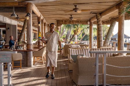A smiling waiter carrying a tray of colourful cocktails along the deck of one of Kokomo Island Fiji’s oceanfront restaurants.