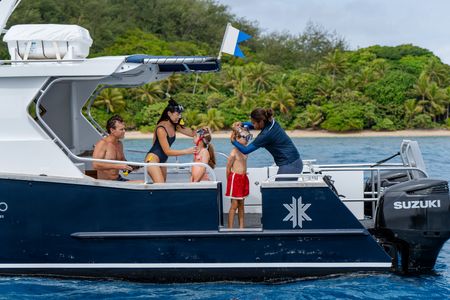 A family putting on snorkeling equipment on one of Kokomo Island Fiji’s boats. One of the parents is helping a child fit their snorkel while a staff member is helping adjust the other child’s goggles.