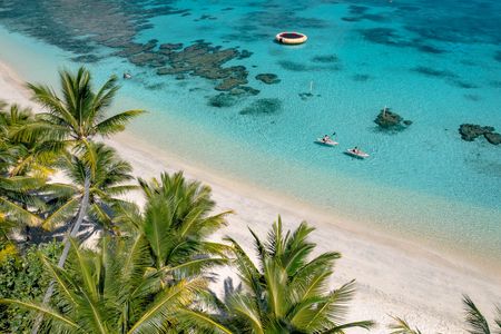 Two guests kayaking near Kokomo Island Fiji’s sandy storeline, with clear, calm waters beneath them. A number of reefs can be seen throughout the waters.