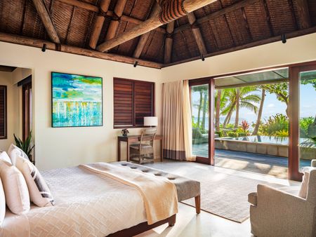 A large bedroom of a villa at Kokomo Island Fiji, with large doors open to the deck area and private infinity pool. The modern room is tastefully designed with Fijian influences.