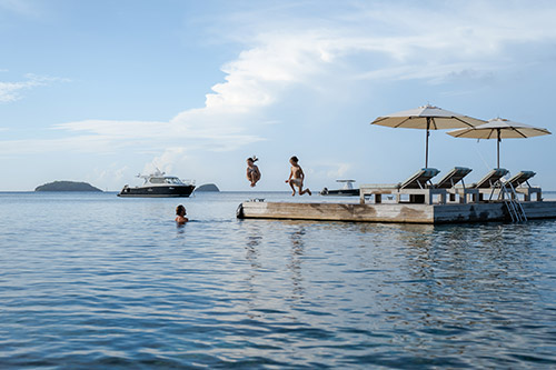 A family swimming and diving off of the floating pontoon at Kokomo Private Island Fiji