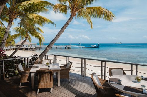 A deck dining area overlooking the white sandy beach and clear blue waters on the shore of Kokomo Private Island Fiji.