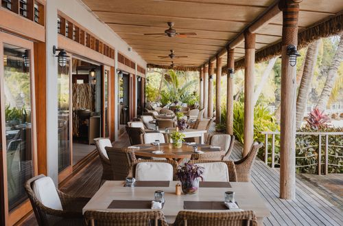 An outdoor dining area at Kokomo Private Island Fiji including several four- to six-seater tables under a spacious awning running alongside the beach.