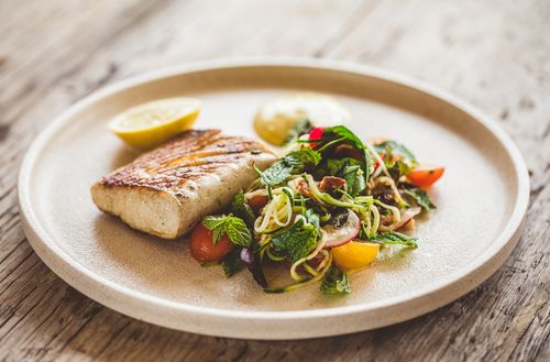 A seared fish fillet with a fresh salad served on a large ceramic plate.